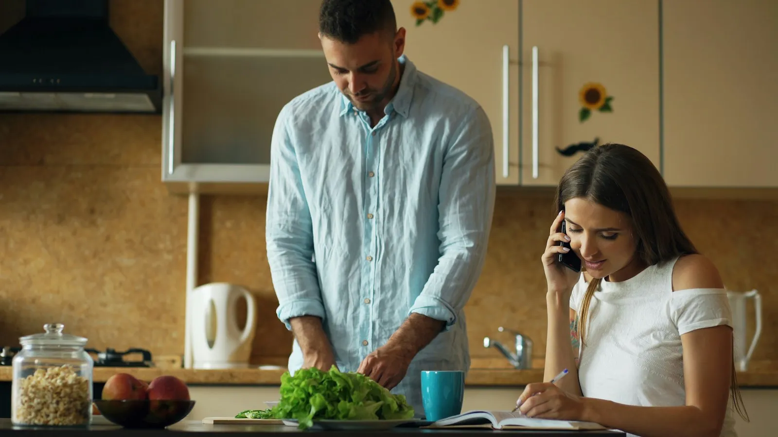 A man chops vegetables in the kitchen while his partner talks on the phone